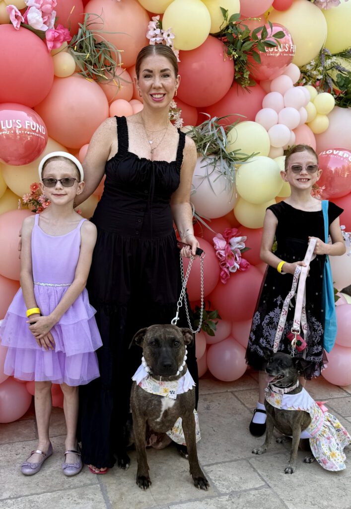 Woman and two children with two dogs at #LovePup Foundation event with pink balloon backdrop